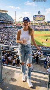 Casual outfit featuring white tank top, ripped jeans, baseball cap, sneakers, sunny outdoor setting, lifestyle photography